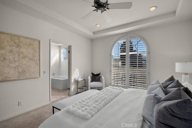 bedroom with ceiling fan, a tray ceiling, light carpet, and ensuite bath