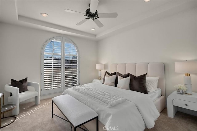 bedroom featuring ceiling fan, a raised ceiling, and light colored carpet