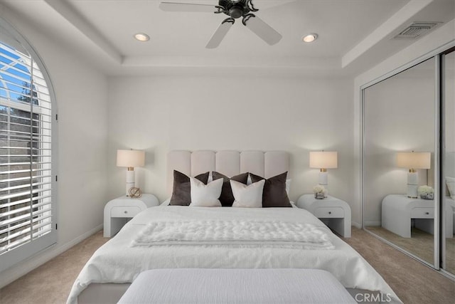 bedroom with a tray ceiling, light colored carpet, a closet, and ceiling fan