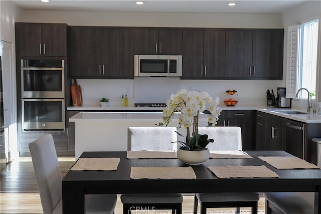 kitchen with sink, light hardwood / wood-style flooring, stainless steel appliances, a center island, and dark brown cabinetry