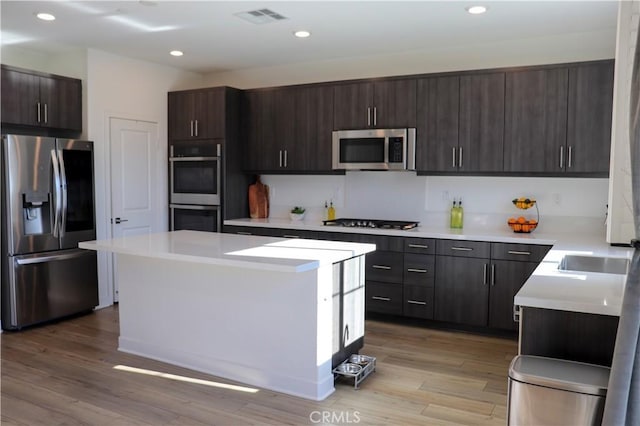 kitchen featuring appliances with stainless steel finishes, a center island, light wood-type flooring, and dark brown cabinets