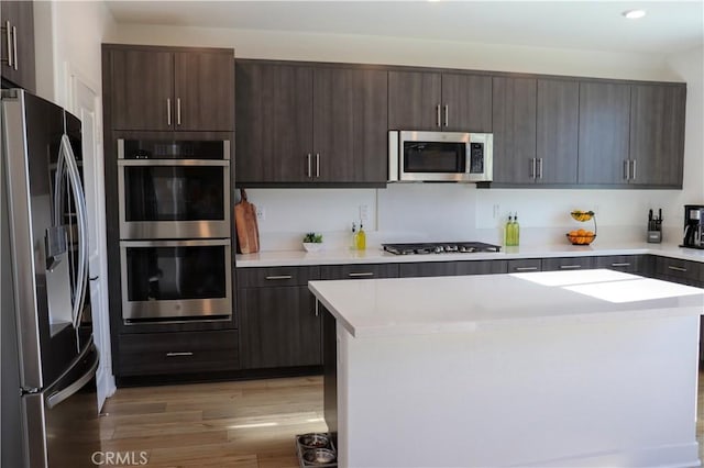 kitchen with dark brown cabinets, a kitchen island, light hardwood / wood-style floors, and appliances with stainless steel finishes