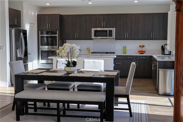 kitchen with sink, dark brown cabinets, light hardwood / wood-style flooring, and appliances with stainless steel finishes