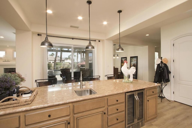 kitchen featuring sink, pendant lighting, beverage cooler, light stone countertops, and light hardwood / wood-style floors