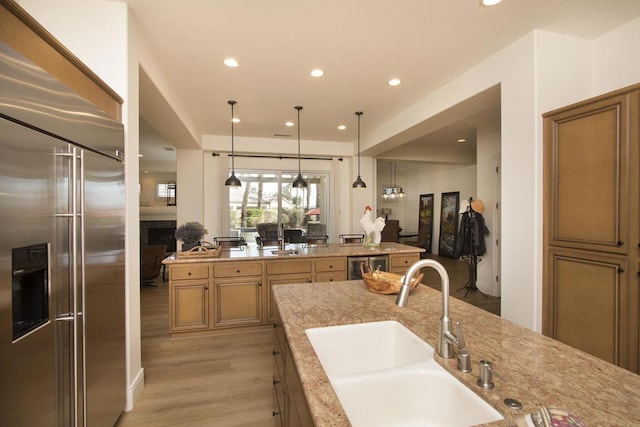 kitchen with pendant lighting, sink, light hardwood / wood-style flooring, light stone countertops, and built in fridge