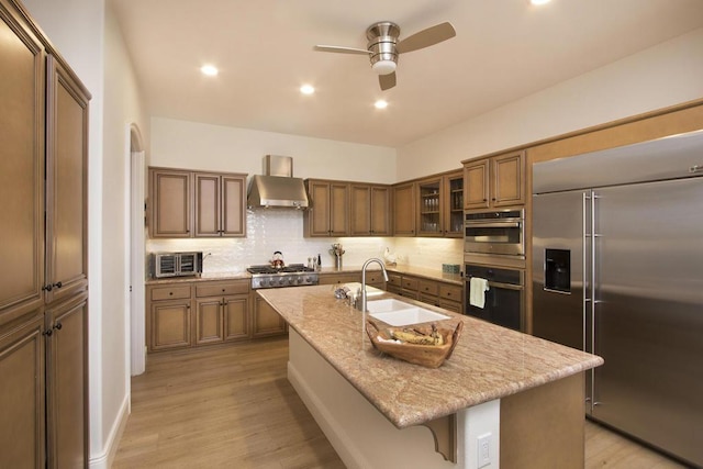 kitchen with stainless steel appliances, an island with sink, sink, and wall chimney exhaust hood