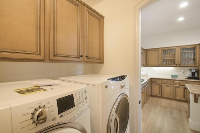 clothes washing area with cabinets, washer and clothes dryer, and light hardwood / wood-style flooring