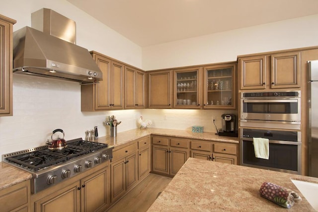 kitchen featuring stainless steel appliances, light stone countertops, light wood-type flooring, and wall chimney range hood