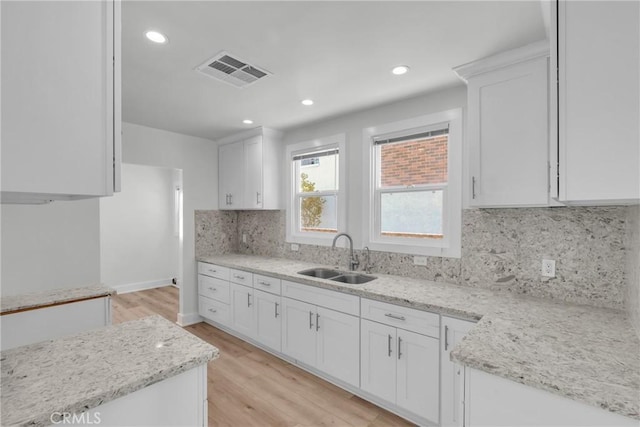 kitchen featuring sink, light hardwood / wood-style flooring, backsplash, light stone counters, and white cabinets