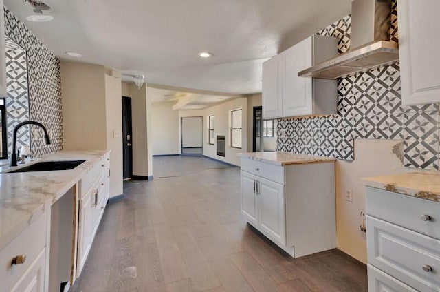 kitchen with white cabinetry, wall chimney range hood, light stone countertops, and sink