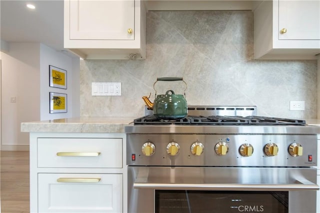 kitchen with white cabinets, wood-type flooring, high end stainless steel range, and backsplash