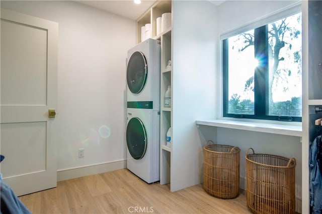 clothes washing area with stacked washer / drying machine, plenty of natural light, and light wood-type flooring