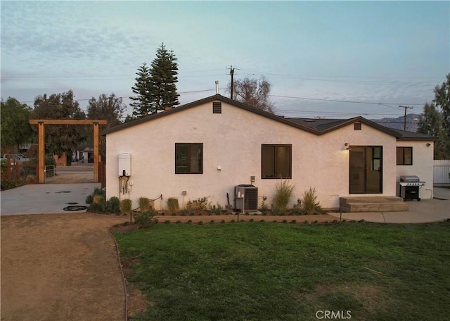 rear view of property with central AC unit and a lawn