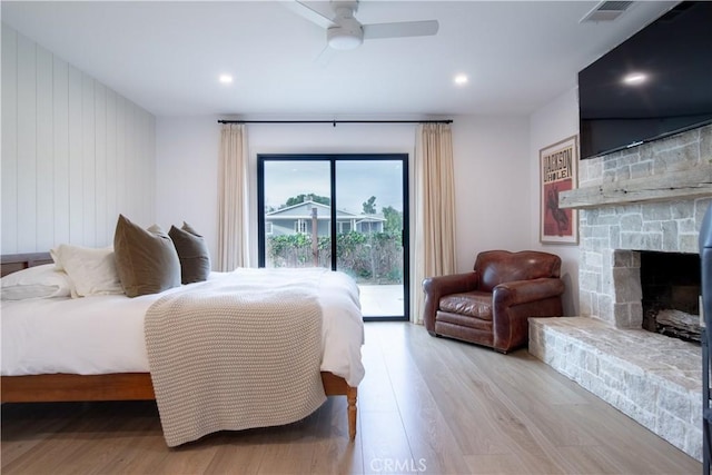 bedroom featuring ceiling fan, access to exterior, a stone fireplace, and light hardwood / wood-style flooring