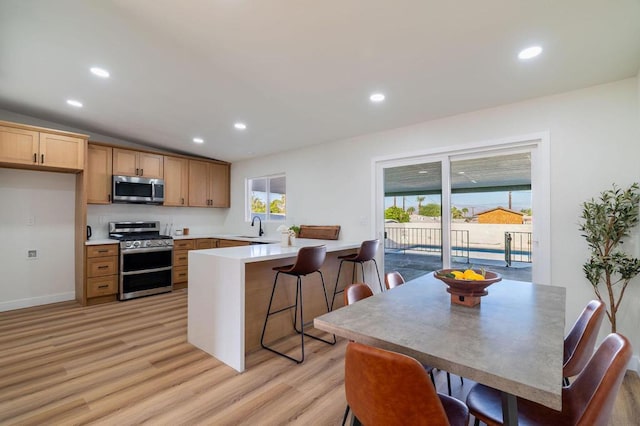 kitchen with lofted ceiling, a kitchen bar, sink, light hardwood / wood-style flooring, and stainless steel appliances