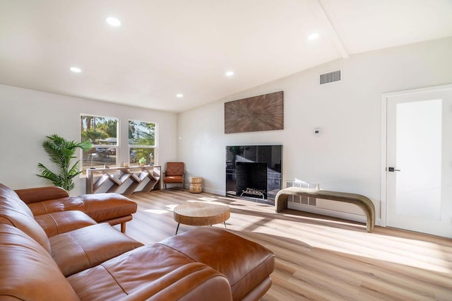 living room featuring a tiled fireplace, vaulted ceiling, and light hardwood / wood-style floors