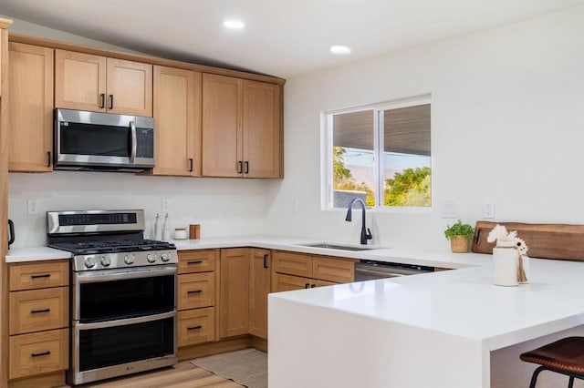 kitchen with sink, a breakfast bar area, appliances with stainless steel finishes, kitchen peninsula, and light hardwood / wood-style floors