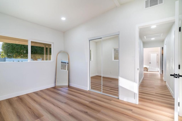 unfurnished bedroom featuring vaulted ceiling, a closet, and light wood-type flooring