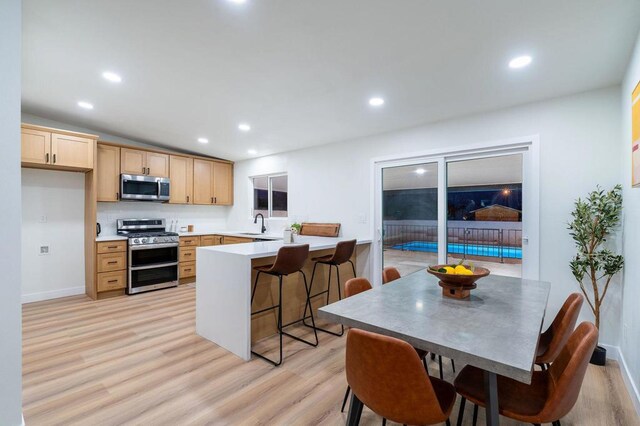 kitchen with light brown cabinetry, a breakfast bar area, vaulted ceiling, light wood-type flooring, and appliances with stainless steel finishes