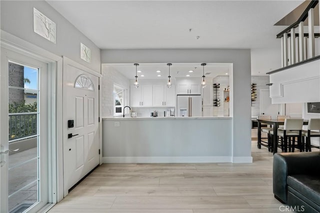 kitchen featuring high end white fridge, white cabinetry, hanging light fixtures, kitchen peninsula, and light wood-type flooring