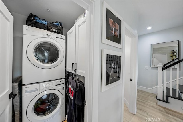 washroom featuring cabinets, light hardwood / wood-style flooring, and stacked washer and clothes dryer