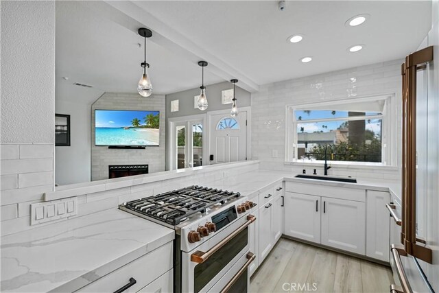 kitchen featuring pendant lighting, sink, white cabinetry, backsplash, and range with two ovens