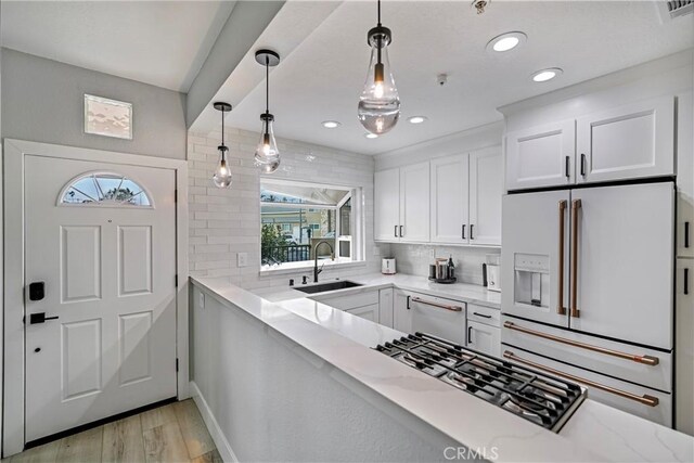 kitchen with sink, tasteful backsplash, pendant lighting, high end white fridge, and white cabinets