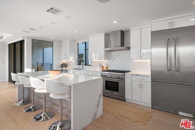 kitchen with wall chimney range hood, sink, white cabinets, and high quality appliances