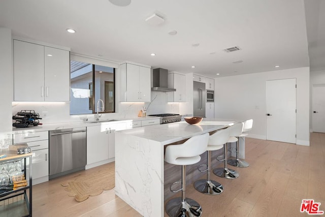 kitchen featuring sink, appliances with stainless steel finishes, a center island, white cabinets, and wall chimney exhaust hood