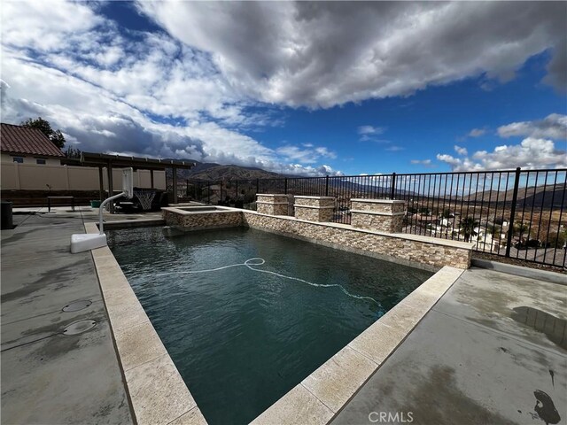 view of swimming pool featuring a pool with connected hot tub, a patio area, fence, and a mountain view