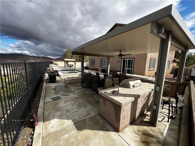 view of patio / terrace featuring ceiling fan, a fenced backyard, exterior kitchen, a bar, and a mountain view