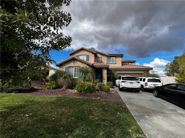 mediterranean / spanish house featuring an attached garage, driveway, a front yard, and stucco siding