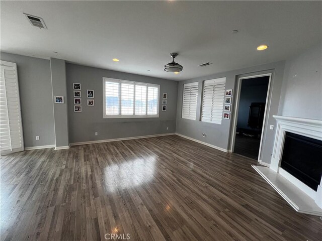 unfurnished living room with dark wood-style floors, visible vents, a fireplace with raised hearth, and baseboards