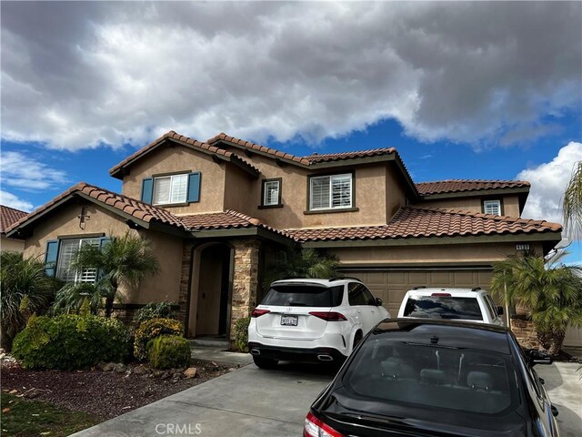 mediterranean / spanish-style house featuring driveway, stone siding, an attached garage, and stucco siding