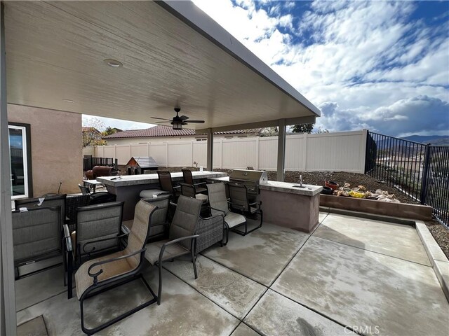 view of patio with ceiling fan, a fenced backyard, outdoor dry bar, a grill, and exterior kitchen