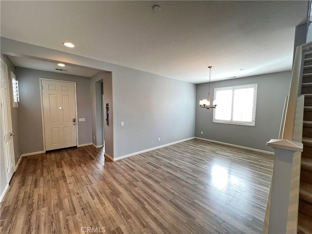 unfurnished room with stairs, light wood finished floors, a notable chandelier, and baseboards