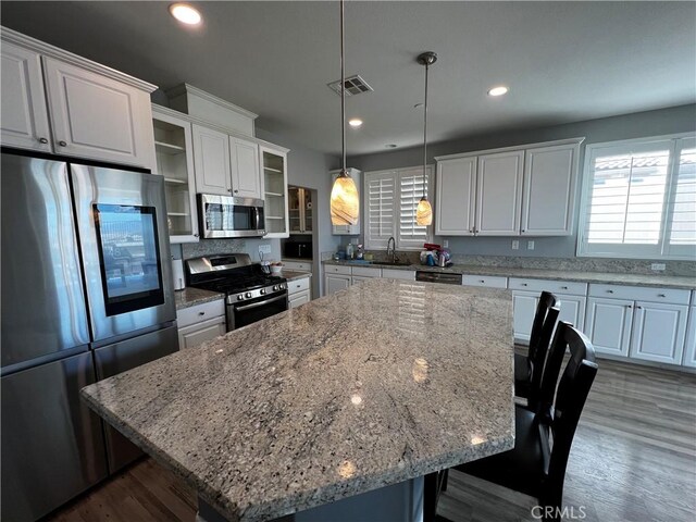 kitchen featuring a breakfast bar, a spacious island, white cabinetry, appliances with stainless steel finishes, and glass insert cabinets