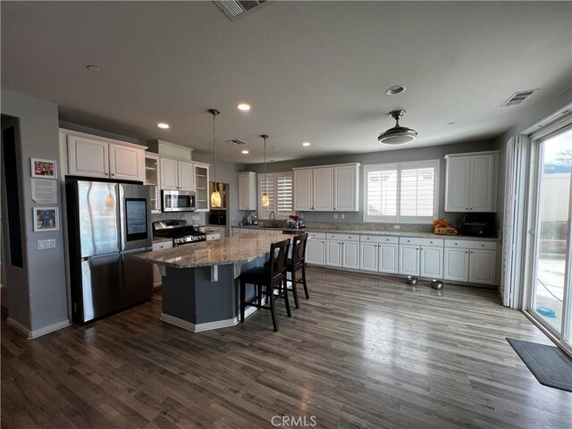 kitchen with appliances with stainless steel finishes, a kitchen island, white cabinetry, and decorative light fixtures