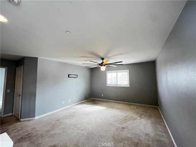 empty room with carpet floors, a ceiling fan, and baseboards