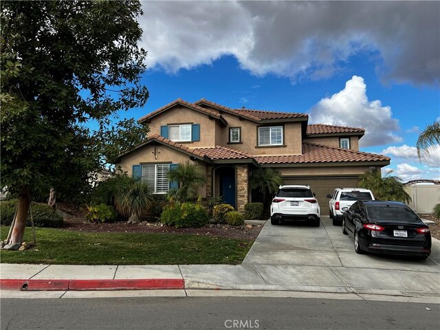 mediterranean / spanish-style house featuring an attached garage, a tile roof, concrete driveway, and stucco siding