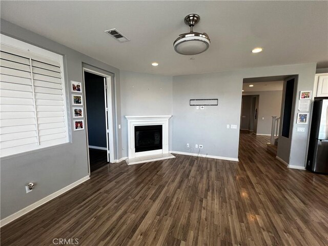 unfurnished living room featuring dark wood-style flooring, visible vents, a fireplace with raised hearth, and baseboards