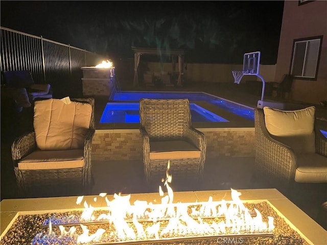 pool at night with an outdoor fire pit, fence, and a hot tub