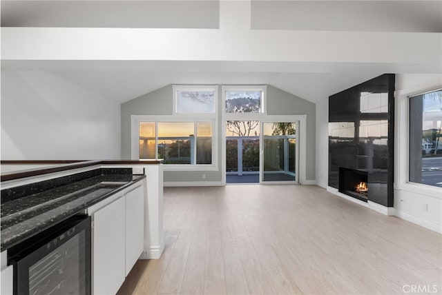 kitchen featuring wine cooler, vaulted ceiling, light wood-type flooring, a large fireplace, and white cabinets