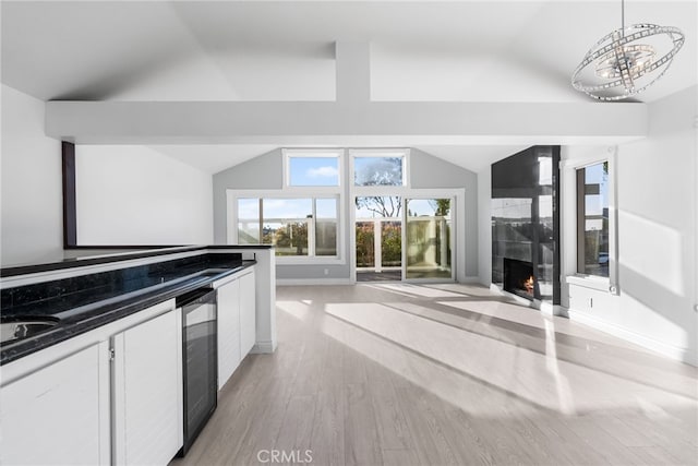 kitchen with a fireplace, vaulted ceiling, pendant lighting, beverage cooler, and white cabinets