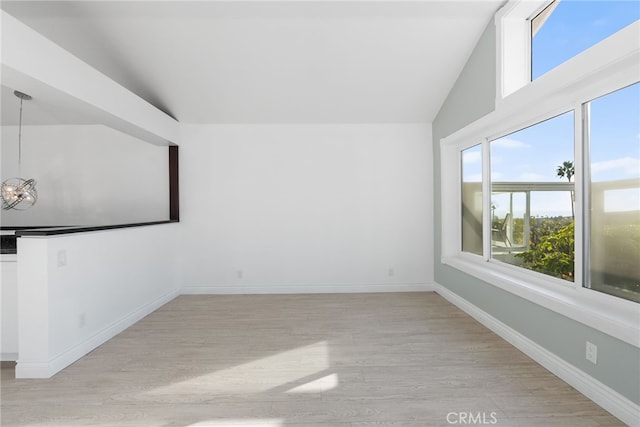 unfurnished room with lofted ceiling, an inviting chandelier, and light wood-type flooring