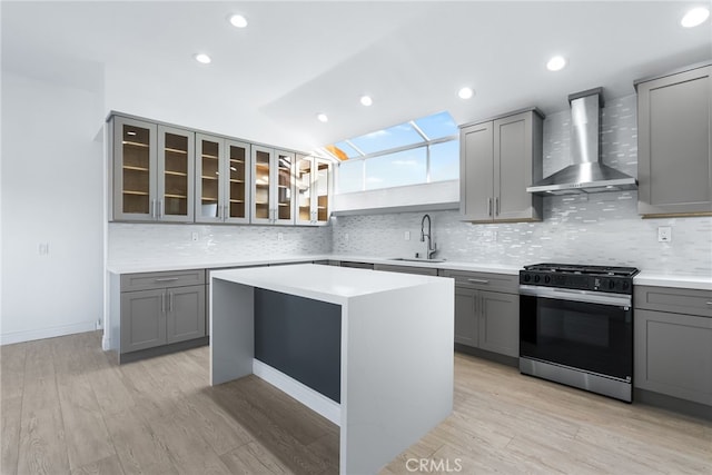 kitchen featuring sink, range with gas cooktop, gray cabinets, a kitchen island, and wall chimney range hood