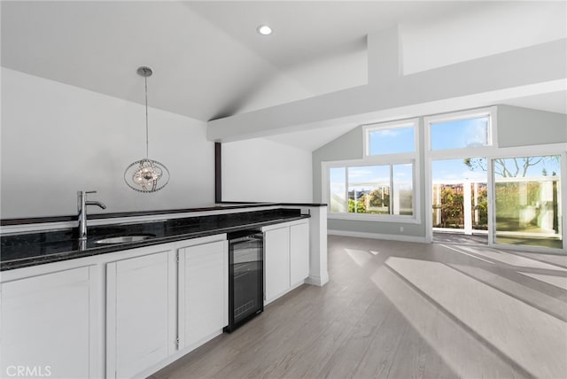 kitchen featuring dark stone countertops, hanging light fixtures, wine cooler, white cabinets, and vaulted ceiling