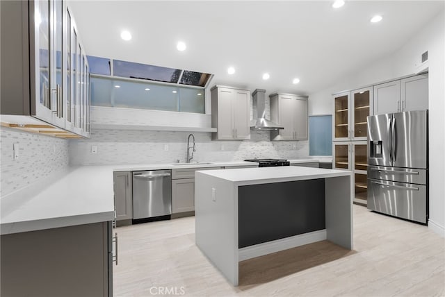 kitchen with sink, appliances with stainless steel finishes, gray cabinetry, a center island, and wall chimney exhaust hood