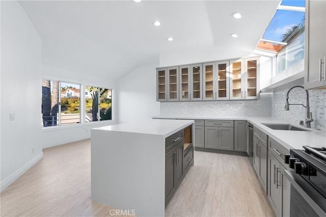 kitchen with lofted ceiling with skylight, sink, a center island, gray cabinets, and range with gas stovetop