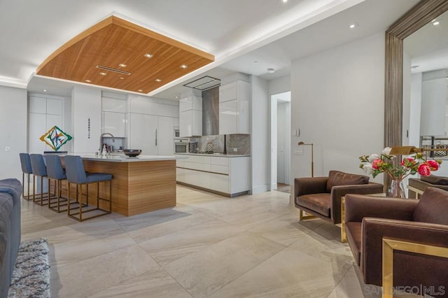 kitchen featuring white cabinetry, stainless steel oven, a center island with sink, wooden ceiling, and decorative backsplash